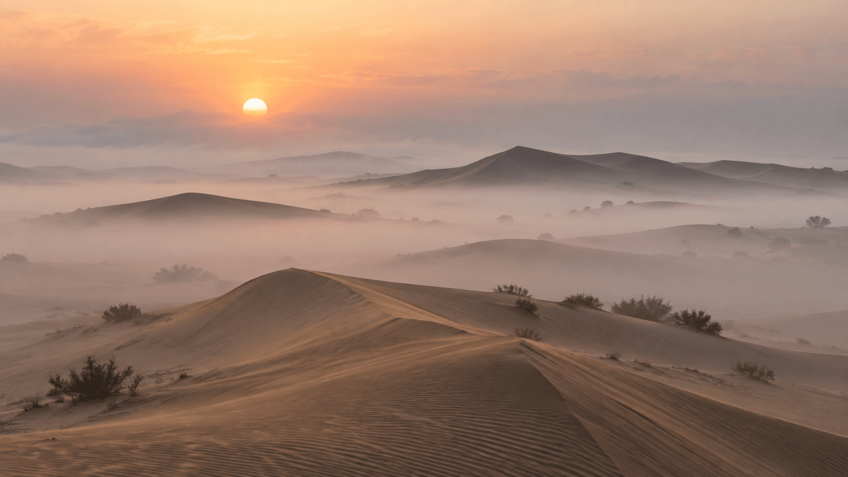 Early morning mist drifting over desert dunes with the sun rising behind